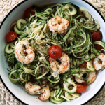 Assiette de spaghettis de courgettes avec crevettes épicées, tomates cerises et olives noires, arrosée d’huile d’olive – plat Paleo léger et coloré.