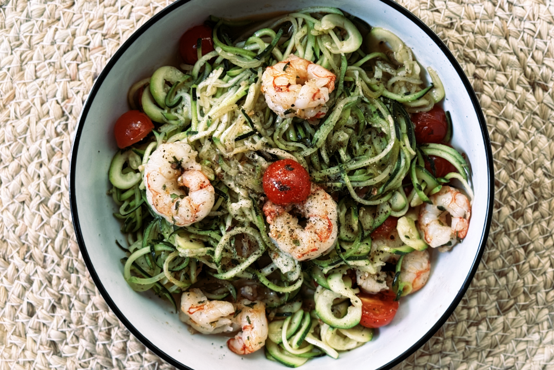 Assiette de spaghettis de courgettes avec crevettes épicées, tomates cerises et olives noires, arrosée d’huile d’olive – plat Paleo léger et coloré.